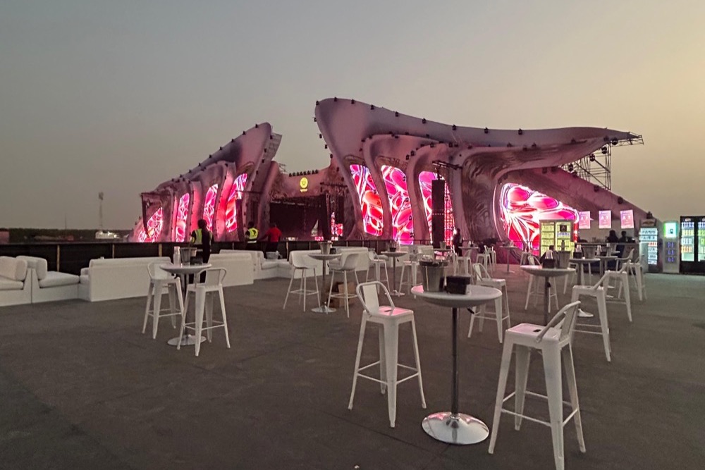 Zona VIP con mesas altas frente a un escenario iluminado al atardecer